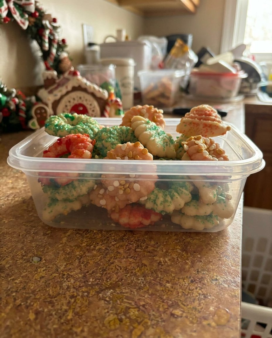 A cookie press being held perpendicular to a cold metal baking sheet while extruding dough.