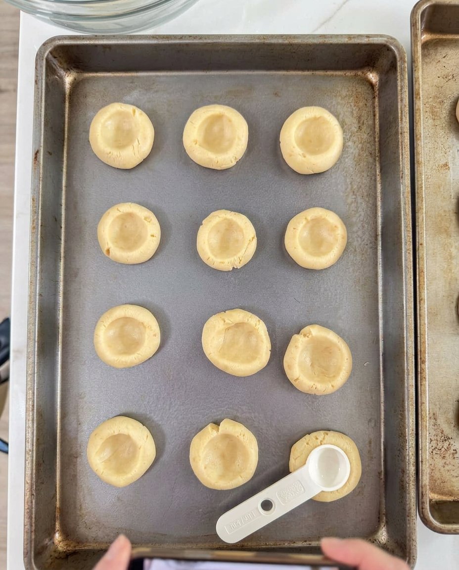 Raw dough balls with thumbprint indentations ready for peach filling.
